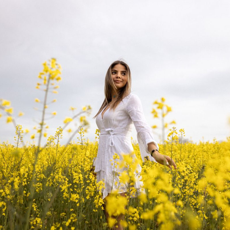 Jeune femme en robe blanche dans un champ de colza en fleurs