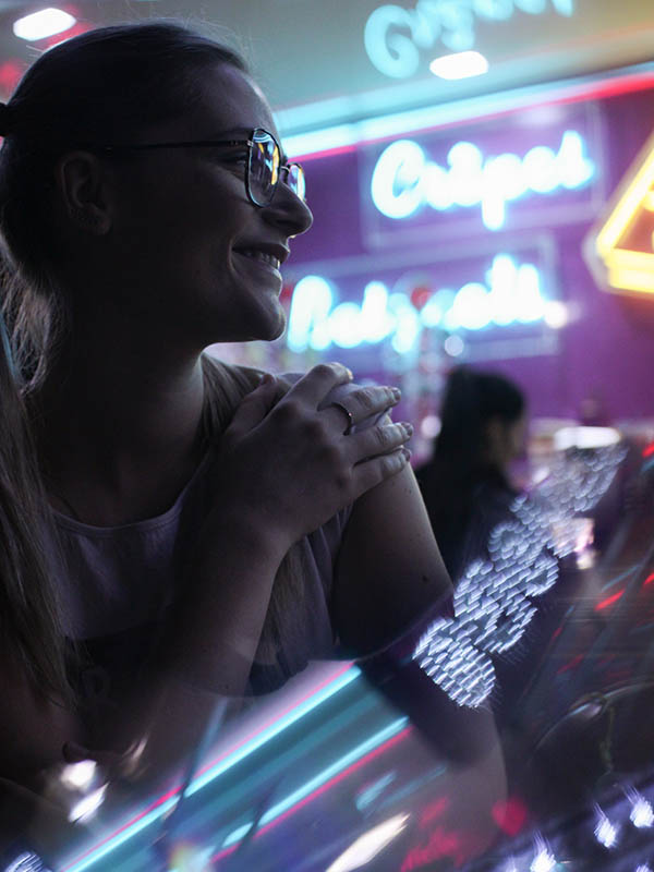 Jeune femme devant les néons d'un stand de crèpes