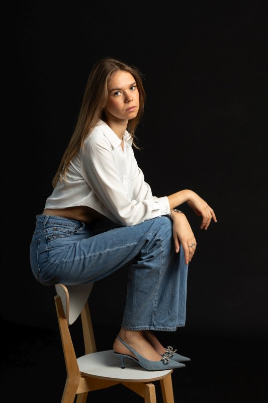 Portrait d'une jeune femme en studio, assise sur une chaise en bois